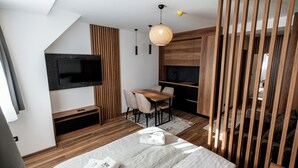 A modern hotel room with a bed, a TV mounted on the wall, a dining table with chairs, and a kitchen area. - Aris KOP Kopaonik (Raška)