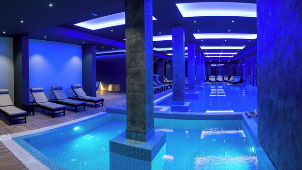 A modern indoor swimming pool with blue lighting, lounge chairs, and a tiled floor. - Aris KOP Kopaonik (Raška)