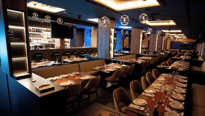 A restaurant with multiple dining tables set for service, a bar area with a variety of bottles, and hanging spherical light fixtures. - Aris KOP Kopaonik (Raška)