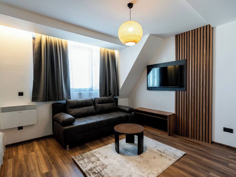 A modern living room with a black leather sofa, a round coffee table, a flat-screen TV mounted on the wall, and a wooden accent wall.