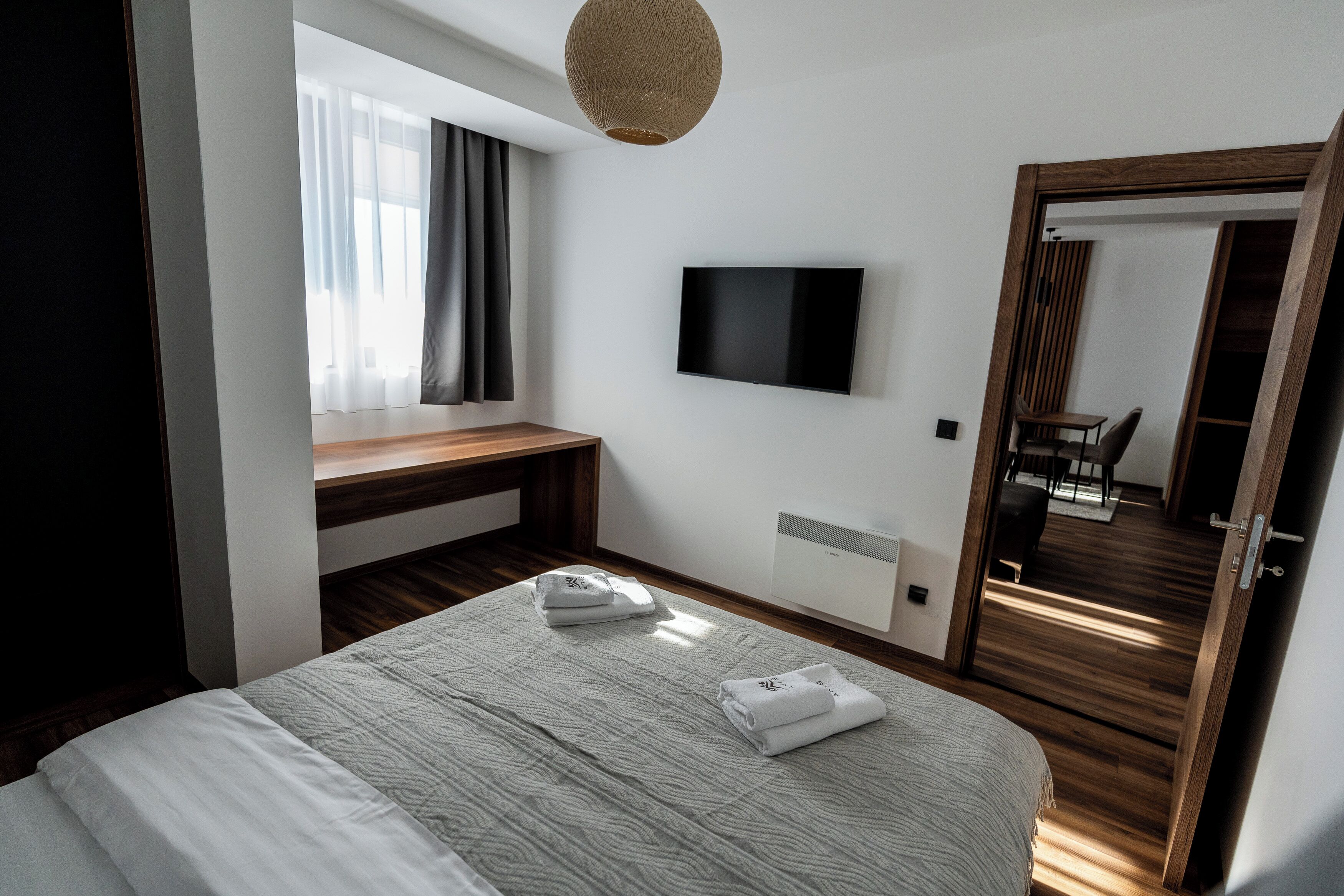 Quarto de hotel moderno com uma cama grande, televisão de tela plana, escrivaninha de madeira e um espelho amplo.