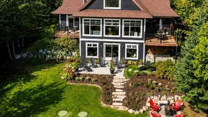 A two-story house with a large deck, surrounded by a well-maintained garden and trees. - Beau Lieu - River View - Spa And Pool Table (Petite-Rivière-Saint-François)
