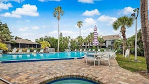 Ein Swimmingpool mit Liegestühlen und einem Whirlpool, umgeben von Palmen und einer Ziegelterrasse.
