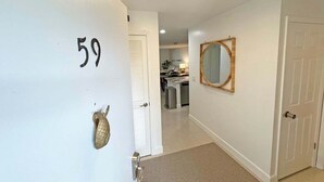 Ein Flur mit der Zahl 59 an der Wand, einer Tür mit Spiegel und einem Küchenbereich im Hintergrund.