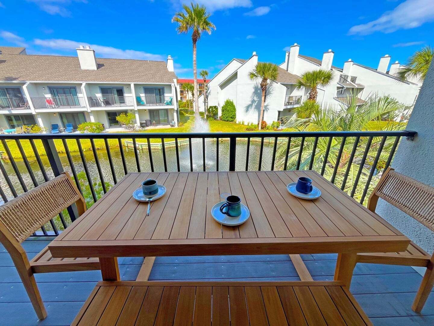 A wooden deck with a table and chairs, overlooking a water body and buildings.