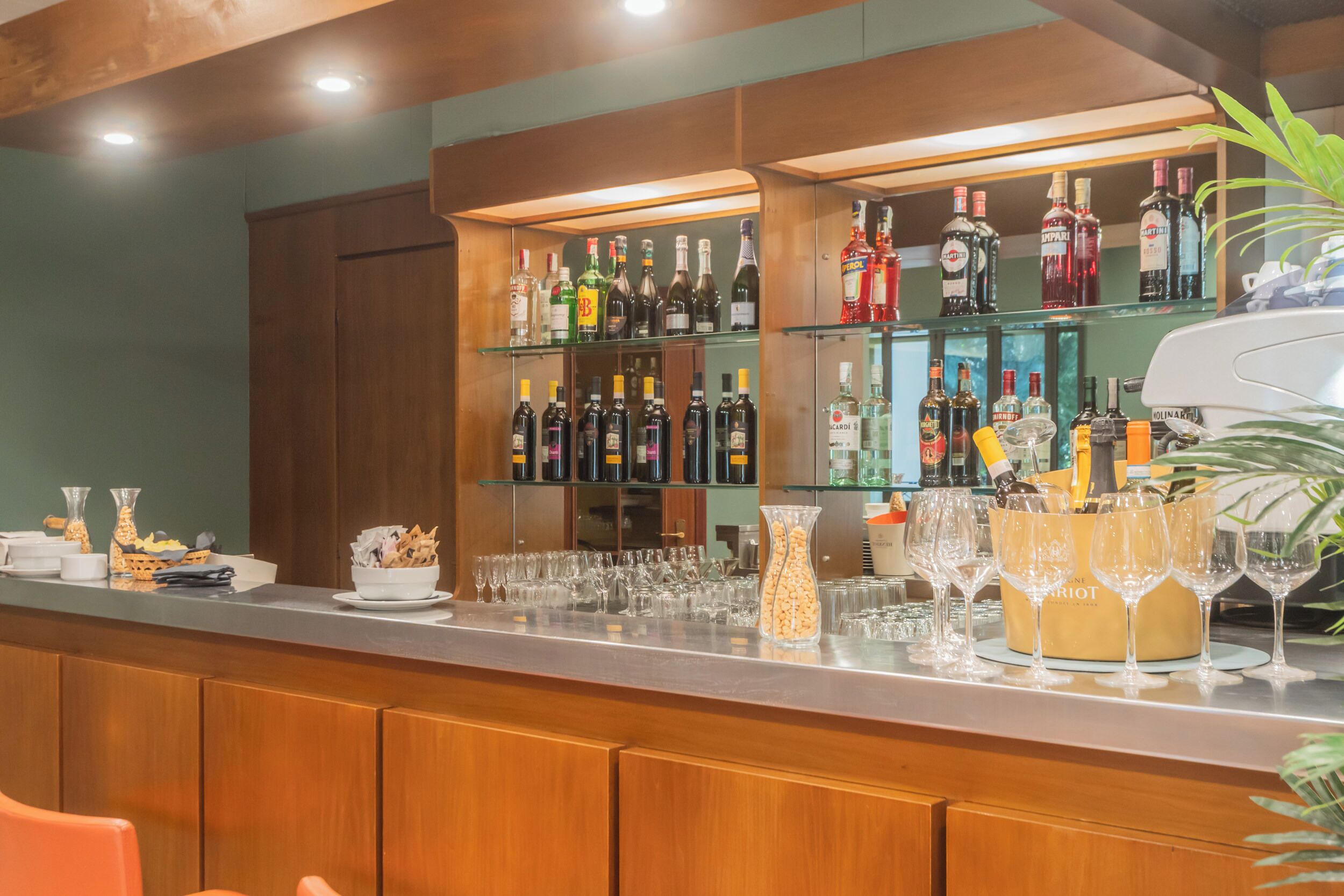A bar area with shelves of liquor bottles, a bar counter, and a plant.