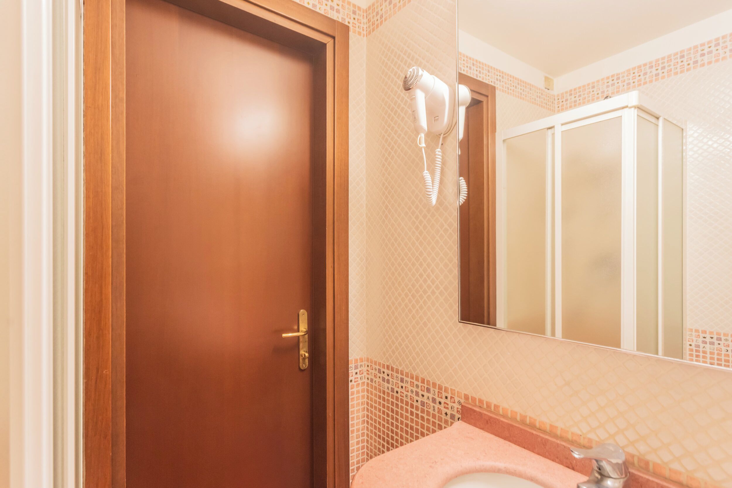 A bathroom with a wooden door, a pink sink, and a hairdryer mounted on the wall.