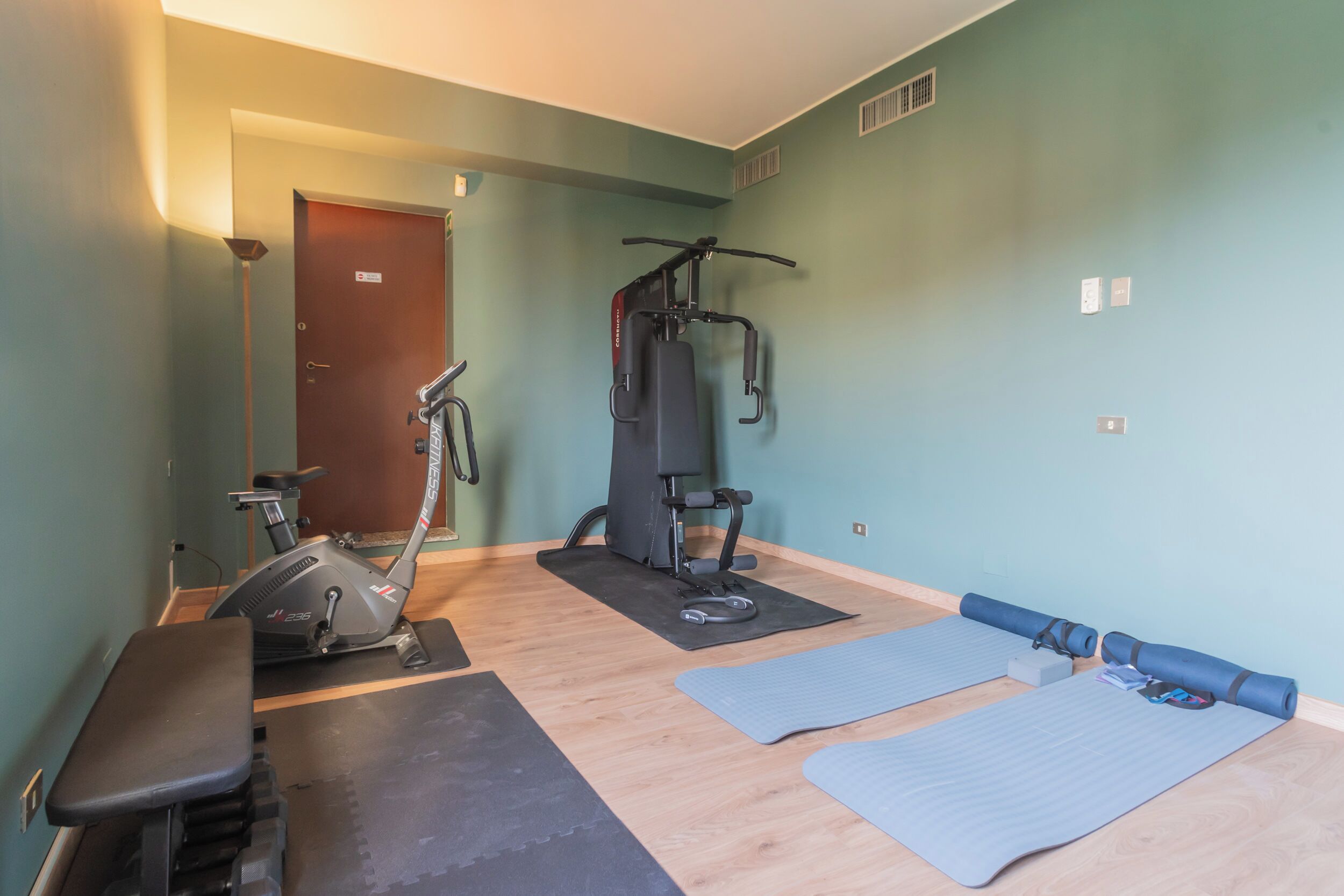 A fitness room with a stationary bike, a multi-functional exercise machine, and yoga mats.