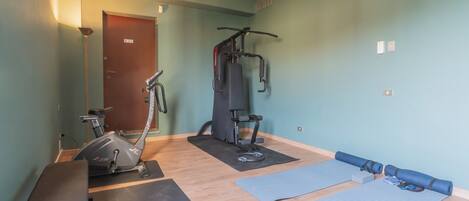 A fitness room with a stationary bike, a multi-functional exercise machine, and yoga mats.
