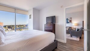Ein Hotelzimmer mit einem großen Bett, einem Fernseher auf einer Kommode, Blick auf die Stadt und einem modernen Design.
