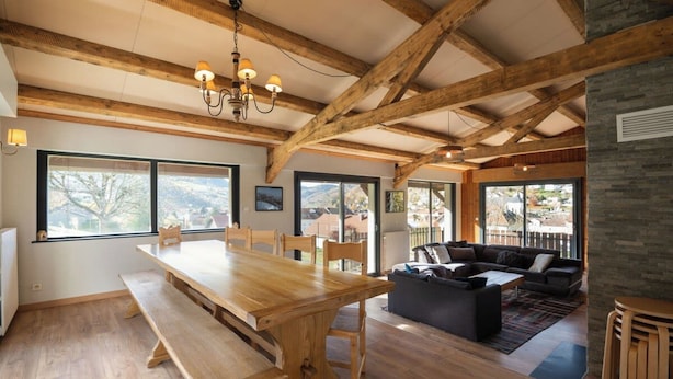 Une pièce spacieuse avec une table à manger en bois, un canapé et une grande fenêtre donnant sur l’extérieur.