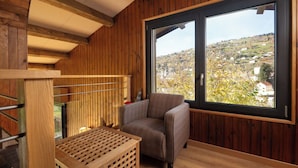 Une pièce aux murs en bois, une grande fenêtre donnant sur la ville, une chaise et une caisse en bois.