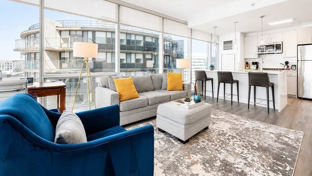 Un appartement moderne comprenant un salon, une cuisine et de grandes fenêtres donnant sur un immeuble.