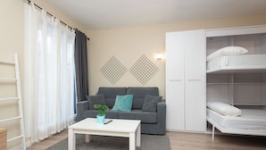 Un salon moderne avec un canapé gris, une table basse blanche et une armoire blanche équipée d’un lit superposé.