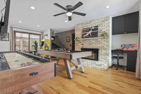 A room with a pool table, a ceiling fan, a brick fireplace, and a desk with a computer.