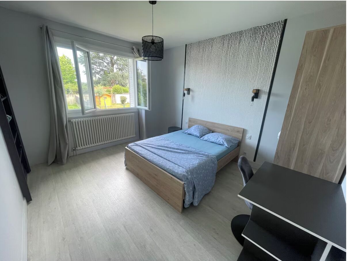 Une chambre à coucher avec un lit, un bureau, un radiateur et une fenêtre avec des rideaux.