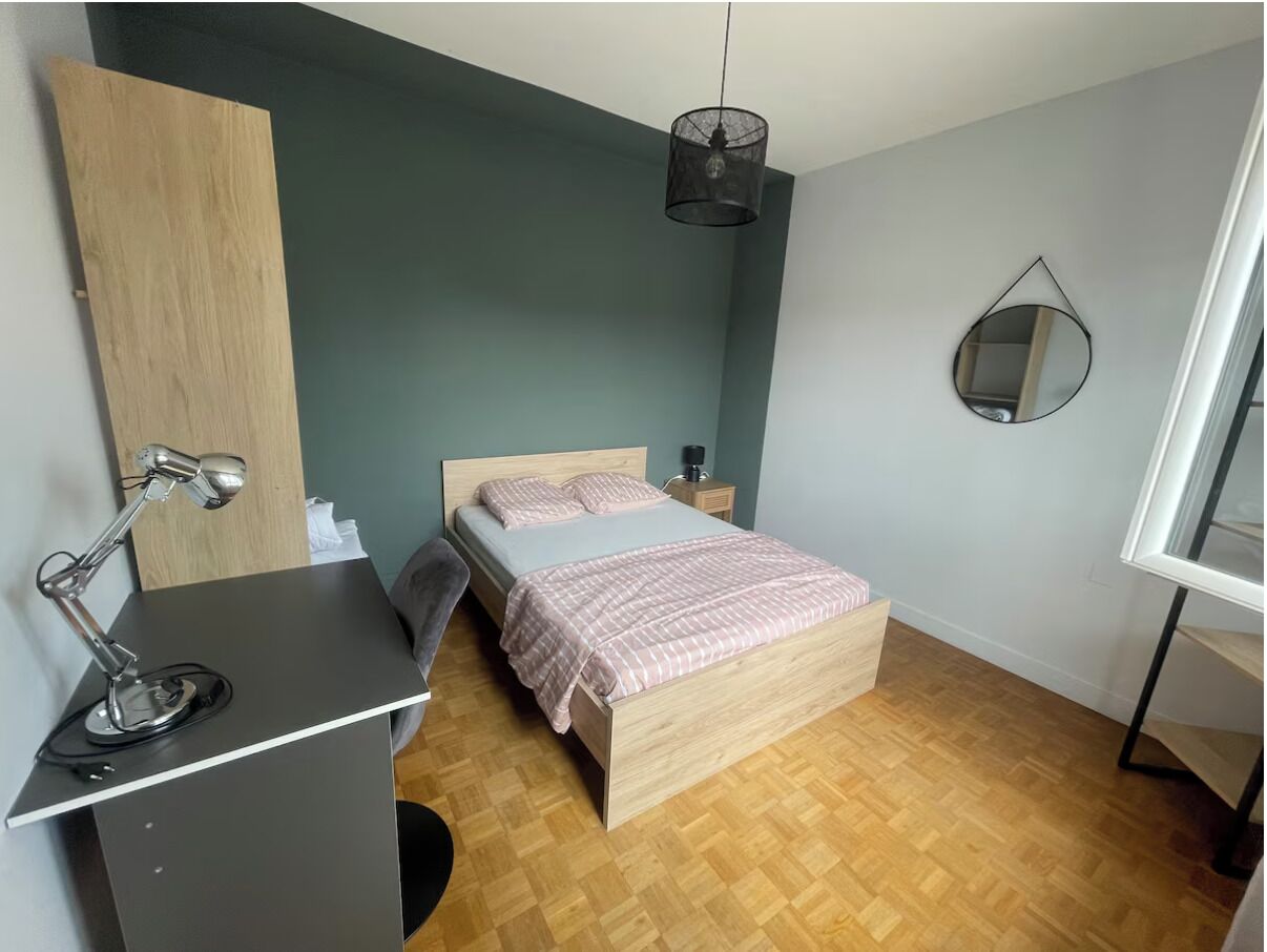 Quarto com cama, mesa de cabeceira, luminária e espelho na parede.