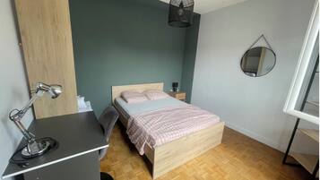 Quarto com cama, mesa de cabeceira, luminária e espelho na parede.