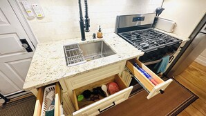 A kitchen with a stainless steel sink, a gas stove, and a built-in oven. There is a small countertop and a cabinet below the sink.