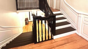 A staircase with black balusters and white walls, leading to a landing with a door and a small table.