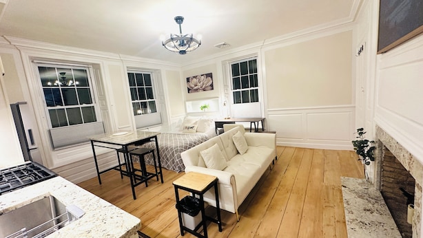 A spacious living room with a white sofa, a dining table, and a kitchen area with a stove.