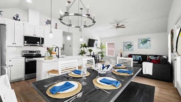 A modern kitchen with white cabinets, a black countertop, and a dining area set for six with a chandelier. - Green Casita, Heated Pool, Fire Pit & Outdoor Bar (Port Aransas)