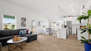 A modern living room with a sofa, coffee table, and dining area. - Green Casita, Heated Pool, Fire Pit & Outdoor Bar (Port Aransas)