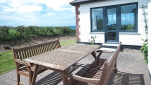 A wooden table and bench set in a garden with a view of the sea. - Chynoweth (Newquay)