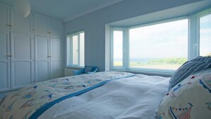 A bedroom with a large bed, a window with blinds, and a white wardrobe. - Chynoweth (Newquay)