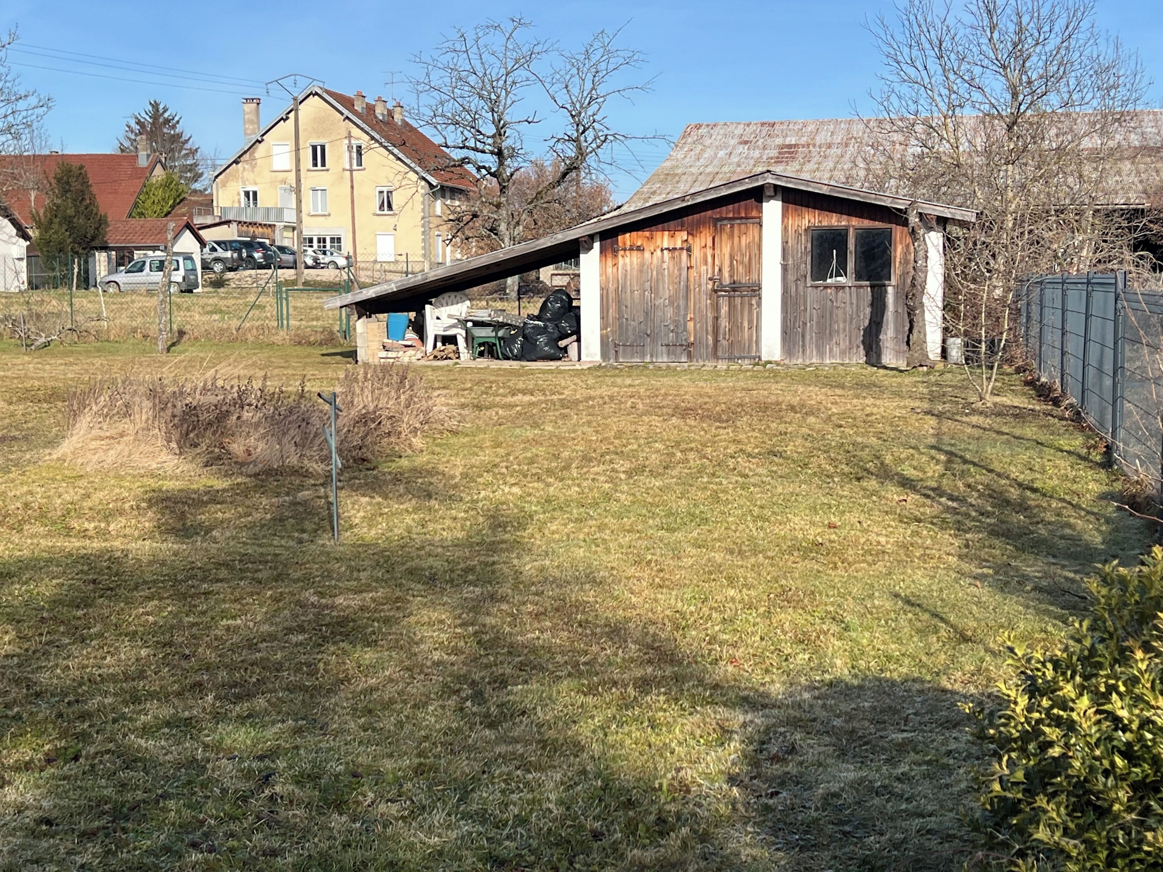 A rural property with a wooden shed, a small garden, and a house in the background.