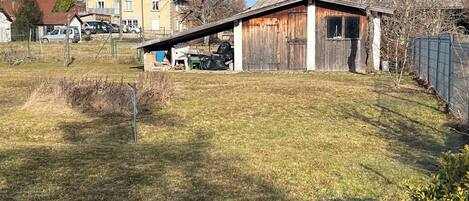 A rural property with a wooden shed, a small garden, and a house in the background.