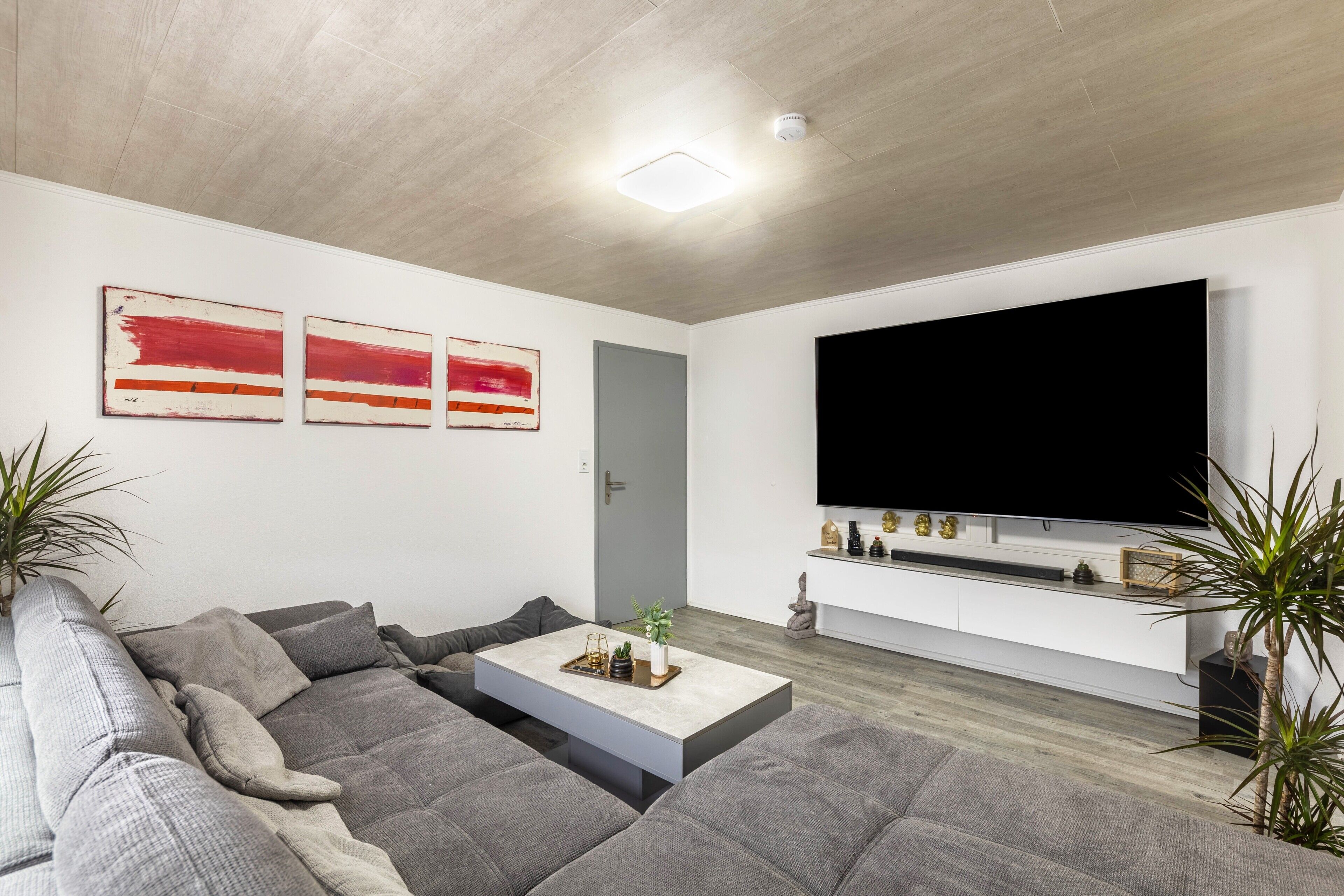 Una sala de estar moderna con un sofá seccional, una mesa de centro, un televisor de pantalla plana montado en la pared y una puerta.