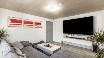 Una sala de estar moderna con un sofá seccional, una mesa de centro, un televisor de pantalla plana montado en la pared y una puerta.