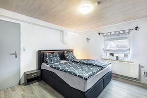 A modern bedroom with a bed, bedside table, and a window with a view. - Apartment 'Klein Frankreich' with Mountain View, Private Terrace and Wi-Fi (Bad Endbach)