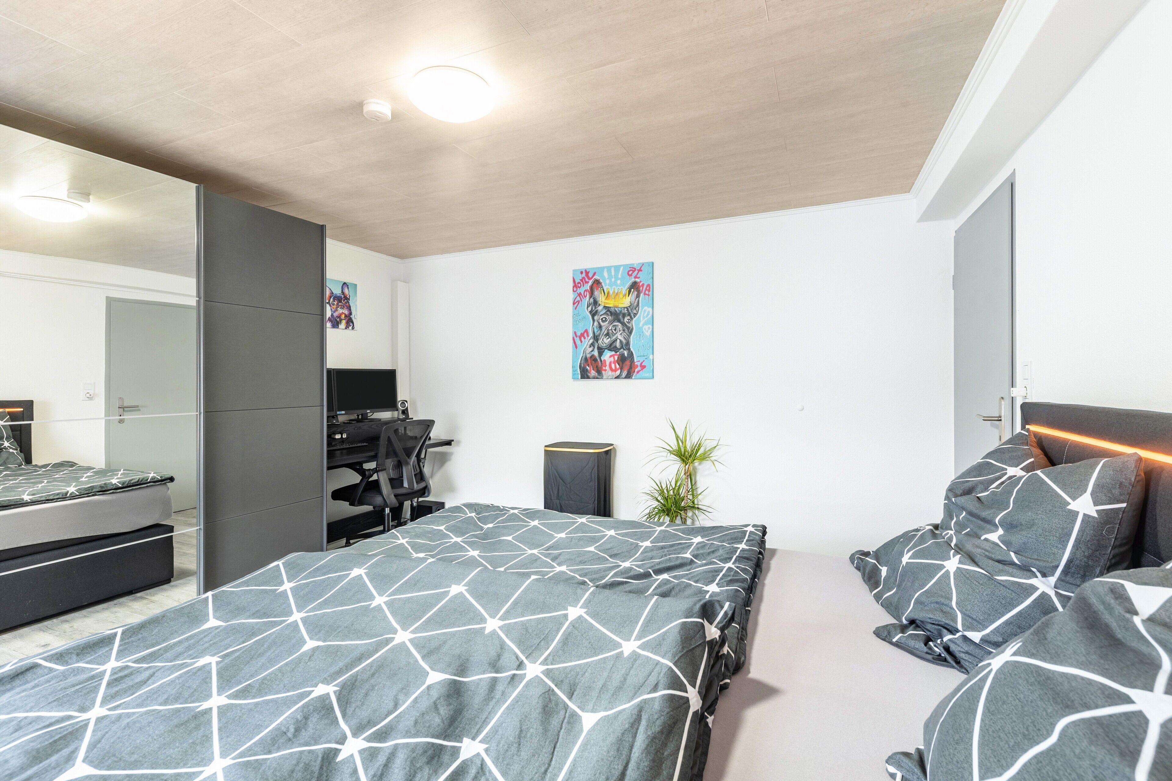 Een moderne slaapkamer met een groot bed, een bureau, een stoel en een kleine plant.