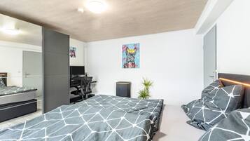 Een moderne slaapkamer met een groot bed, een bureau, een stoel en een kleine plant.