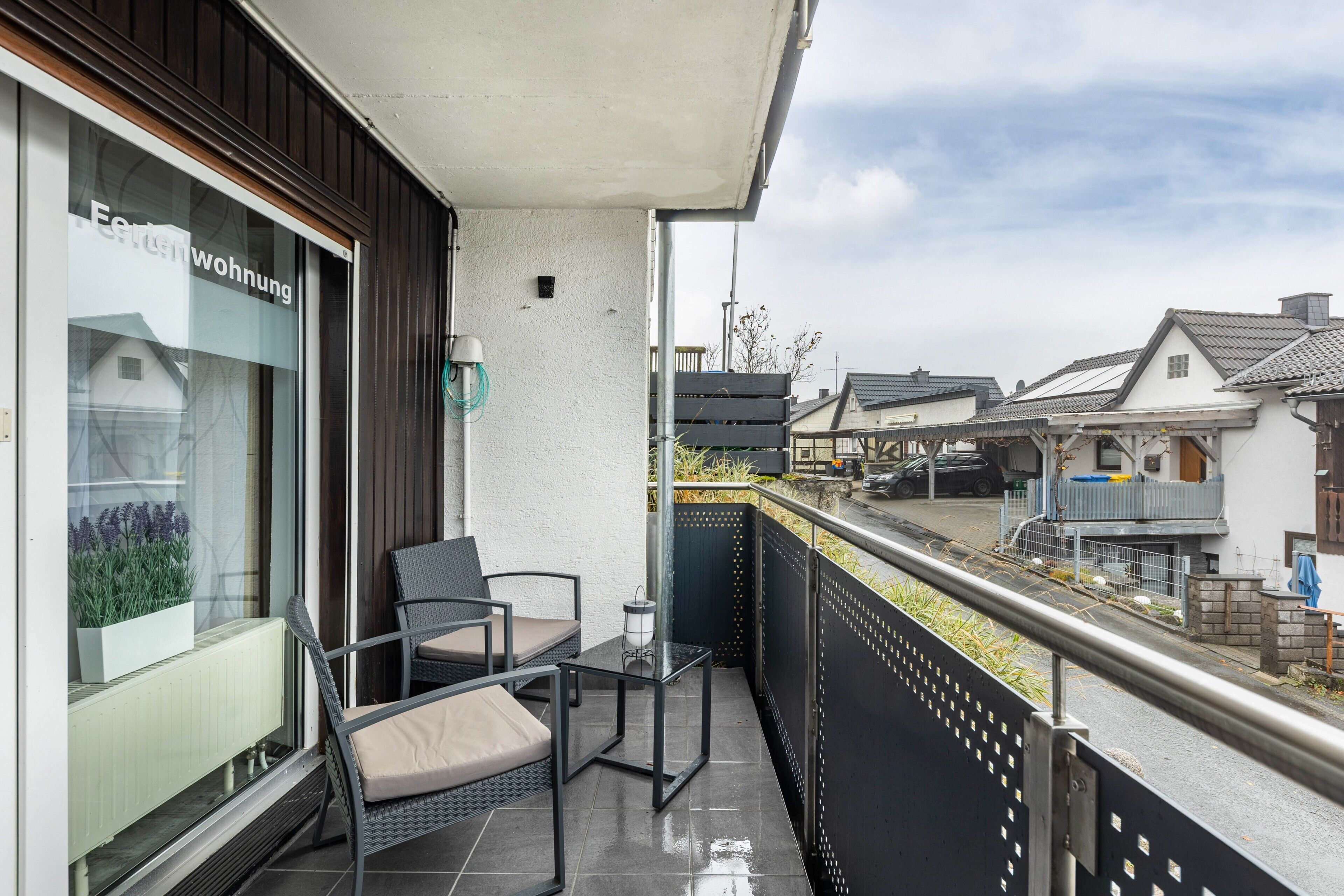 A balcony with wicker furniture, a small table, and a view of traditional houses.