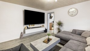 Ein modernes Wohnzimmer mit einem Flachbildfernseher, einem grauen Sofa, einem Couchtisch mit Dekoration und einer Wanduhr.