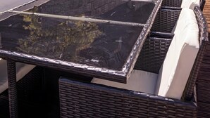 Eine Terrasse mit Glastisch, Korbstühlen, einem Grill und einer Steinmauer mit Kakteen.