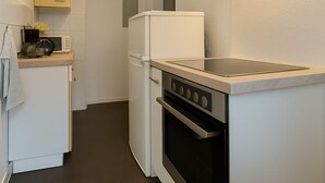 A compact kitchen with white cabinetry, a built-in oven, a microwave, and a stainless steel range hood.