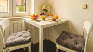 A small dining area with a white table and two chairs, a window with a view of buildings, and a radiator under the table.