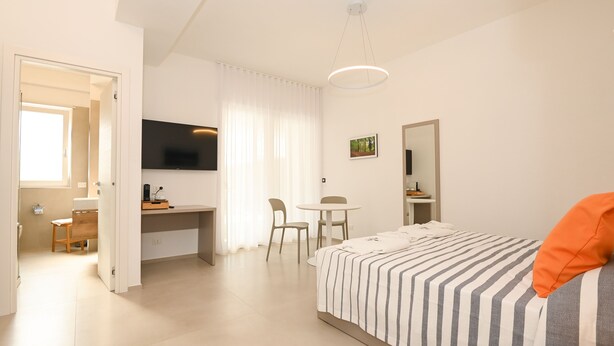 A modern hotel room with a bed, a desk, a chair, a television, and a window with curtains. - Agorà Vieste Rooms & Apartments (Vieste)