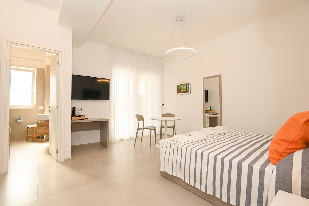 Een moderne hotelkamer met een bed, een bureau, een stoel, een televisie en een raam met gordijnen.