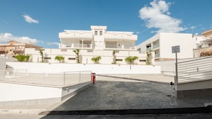 A modern white building with a gated entrance, a paved area, and a clear blue sky. - Agorà Vieste Rooms & Apartments (Vieste)
