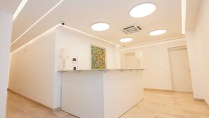 A reception area with a white reception desk, a colorful abstract painting, and a modern ceiling with recessed lighting. - Agorà Vieste Rooms & Apartments (Vieste)