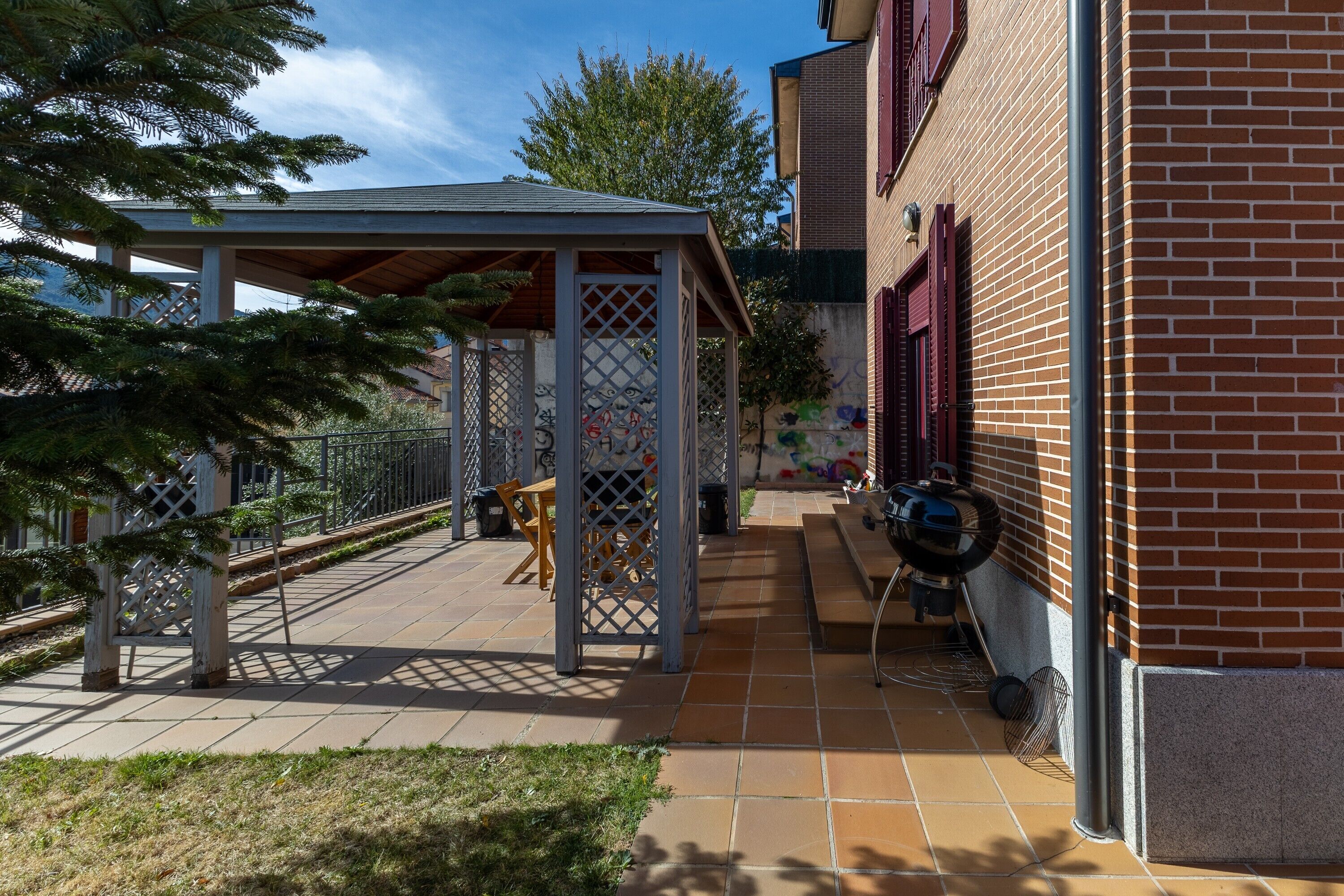 A covered patio area with a wooden bench, a fan, and a grill.