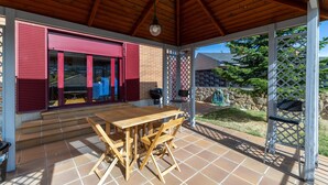 Une terrasse couverte avec une table et des chaises en bois, une porte de garage rouge et une vue sur un quartier résidentiel.