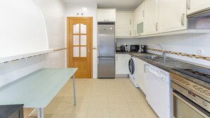 Une cuisine compacte avec des meubles blancs, un réfrigérateur en acier inoxydable, un lave-linge et un lave-vaisselle.