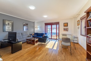 En moderne stue med en grå sofa, et sofabord, et fjernsyn og en bogreol.