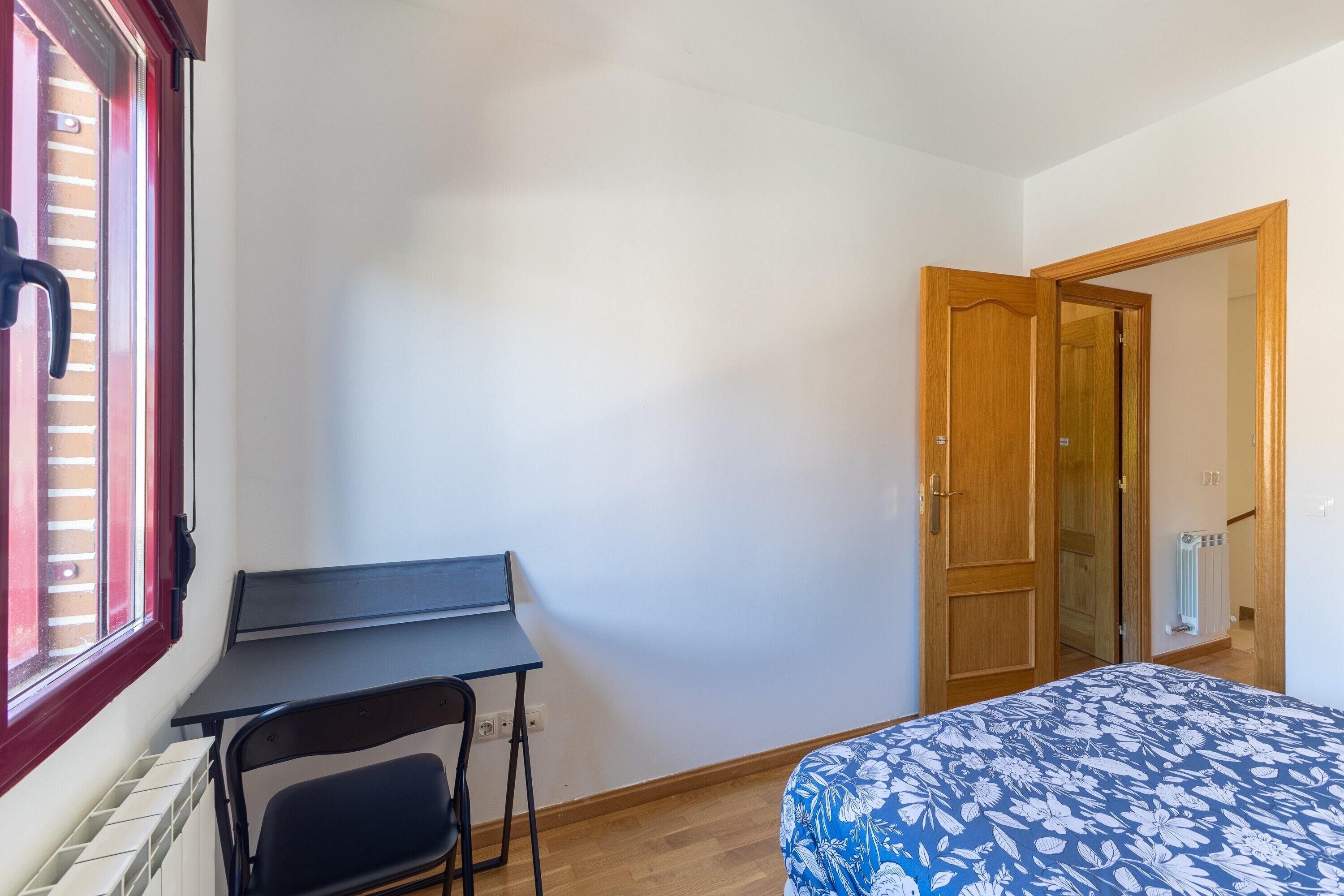 Une chambre à coucher avec un lit, un bureau, une chaise, un radiateur et une porte.